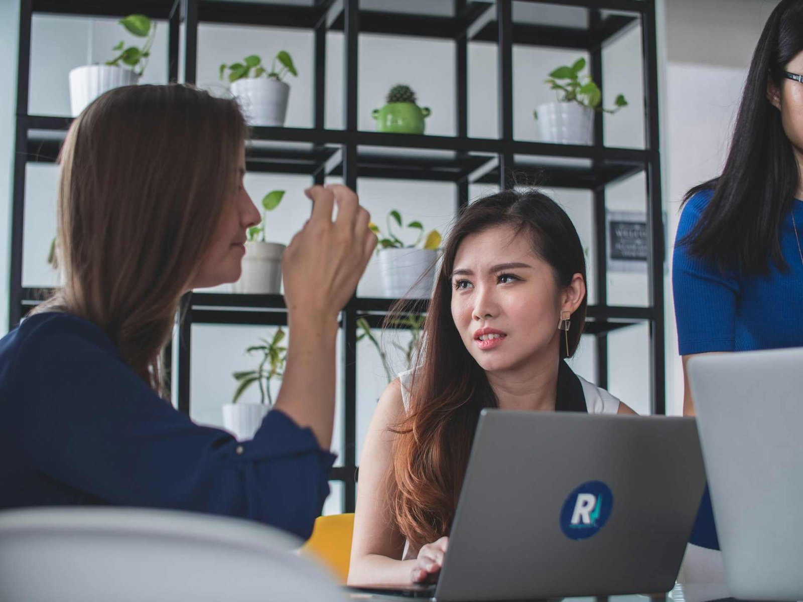 Two women talking to each other at work with the one on the right looking slightly confused at the other.