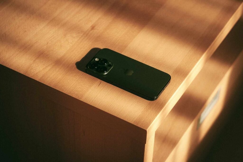 A black apple phone lying face down on a wooden table.